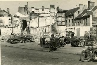 Motocyclistes allemands sur une place de Guise auprès de vestiges de matériel militaire français abandonné après les combats ©Arch. dép. de l’Aisne, 2 Fi 337